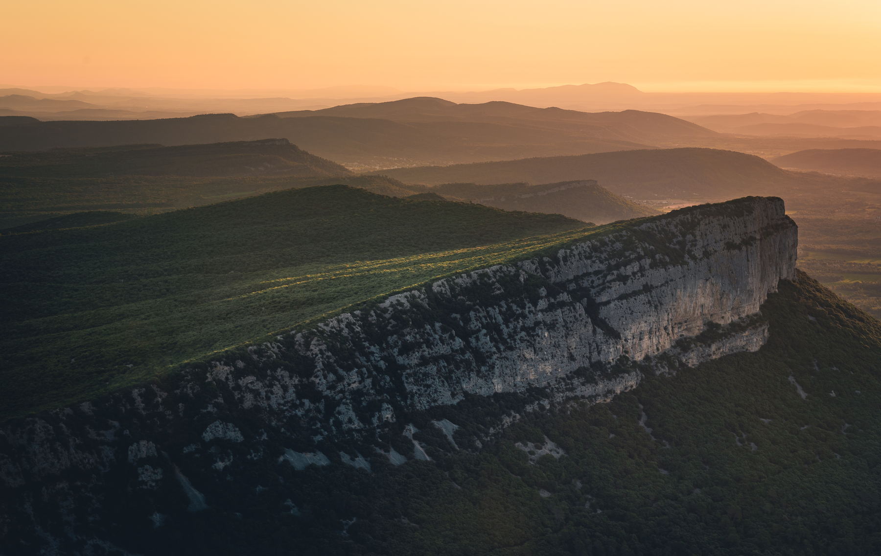 Longue falaise calcaire au lever du jour, reliefs qui s’estompent dans la brume