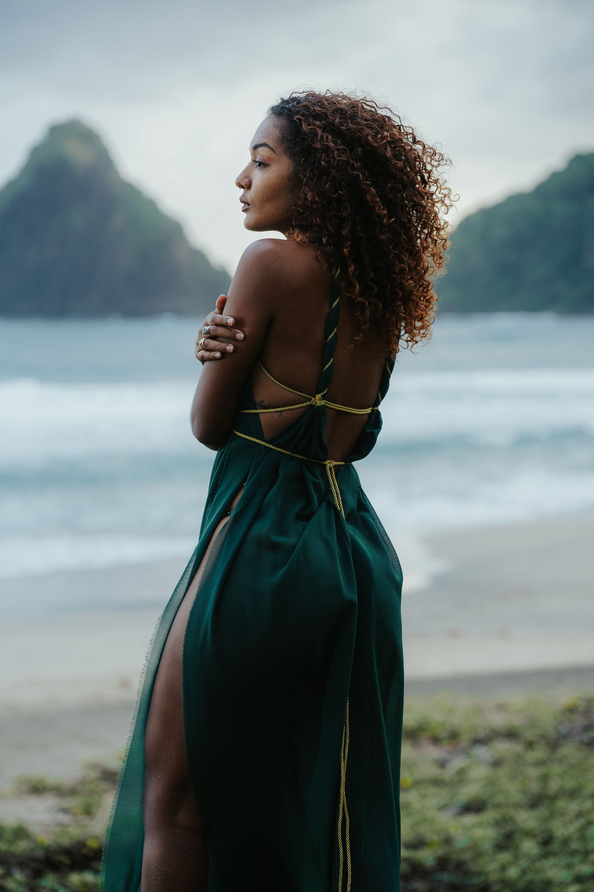 Portrait de dos d'une femme en robe verte sur une plage, piton rocheux dans la brume